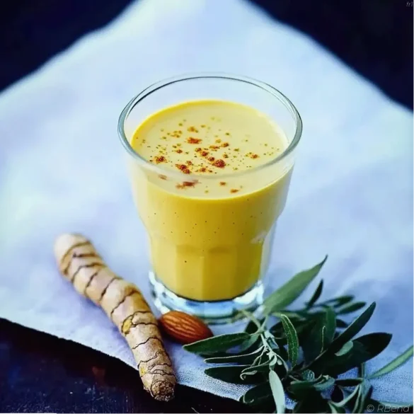 Lait d’or amande curcuma Verre de lait d’or amande curcuma crémeux avec poudre de curcuma en arrière-plan